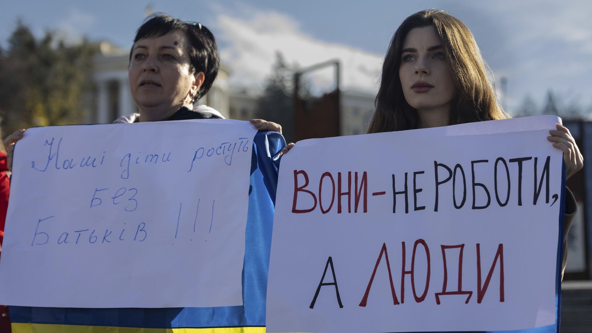 Мария Харченко, справа, которая ждет возвращения своего мужа с передовой, держит плакат с надписью Они не роботы, а люди во время митинга на площади Независимости в Киеве, 27 октября 2023 года. - ИноСМИ, 1920, 18.04.2025